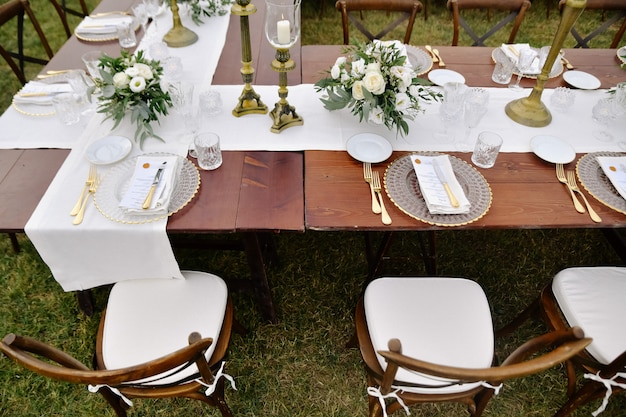 Top view of brown chiavari chairs, glassware and cutlery on the wooden table outdoors, with white eustomas bouquets