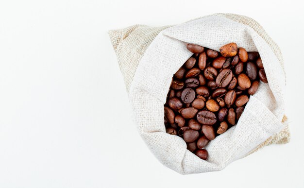コピースペースと白い背景の上の袋に茶色のコーヒー豆のトップビュー