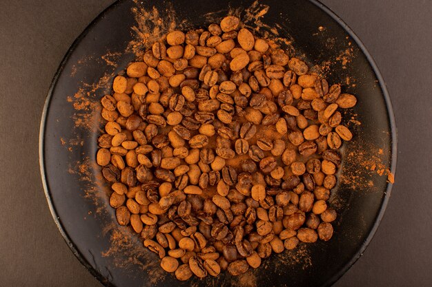 A top view brown coffee seeds inside black plate on the brown table