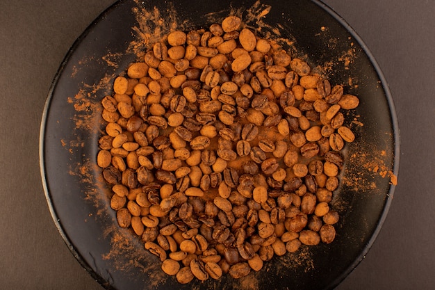 A top view brown coffee seeds inside black plate on the brown table