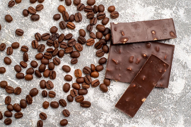 Top view of brown coffee seeds with chocolate bars on a white surface