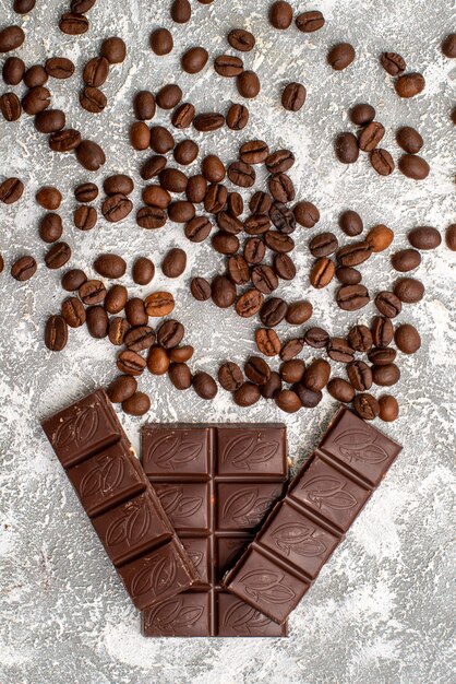 Top view of brown coffee seeds with chocolate bars on the white surface