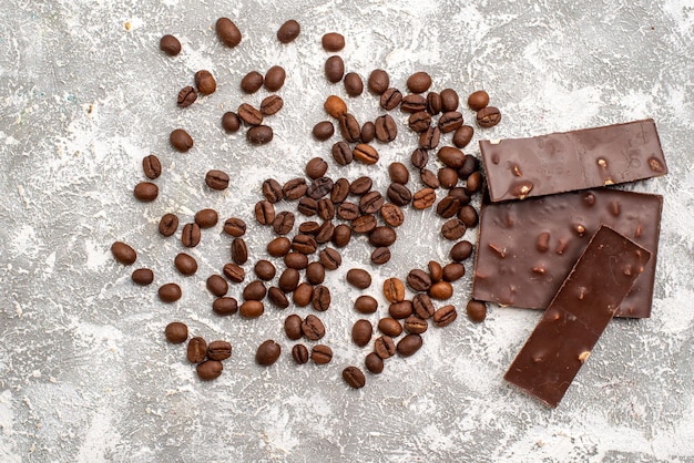 Vista dall'alto di semi di caffè marrone con barrette di cioccolato sulla superficie bianca