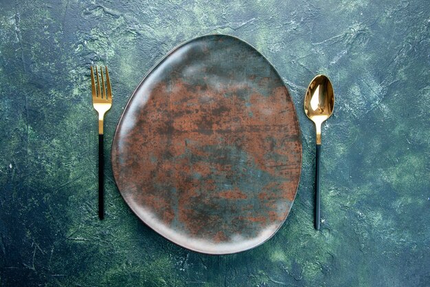 вид сверху коричневая тарелка с золотой ложкой и вилкой на темном фоне цветные столовые приборы ресторан еда кухня посуда ужин обед