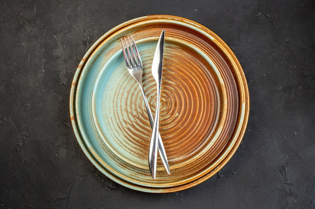 Бесплатное фото Вид сверху коричневые тарелки с вилкой и ножом на темной поверхности