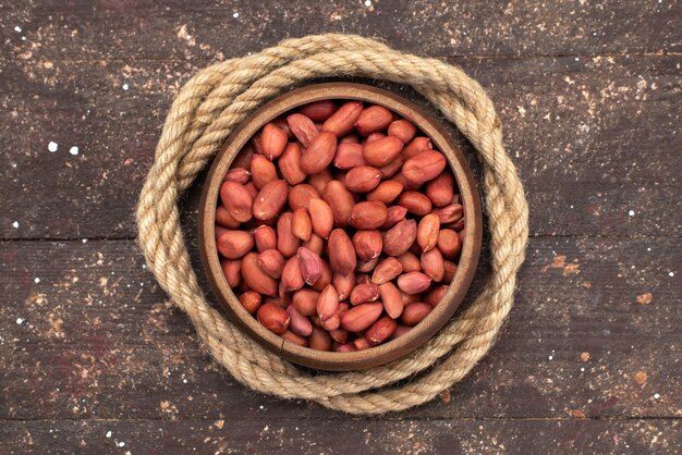 Top view brown raw nuts inside round bowl with ropes on brown, nut walnut snack salt