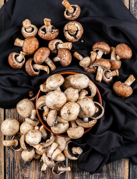 Вид сверху коричневые и белые грибы в миске на черной ткани