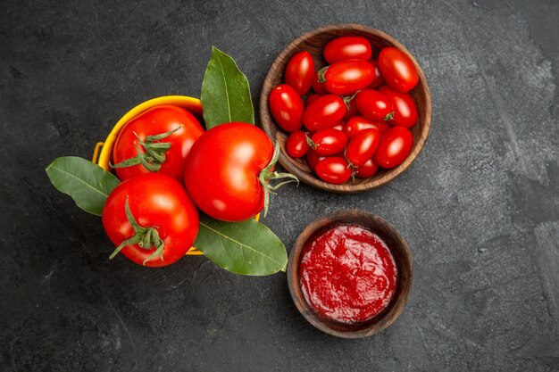 Top view a bucket with tomatoes bowls with cherry tomatoes and ketchup on dark ground py space