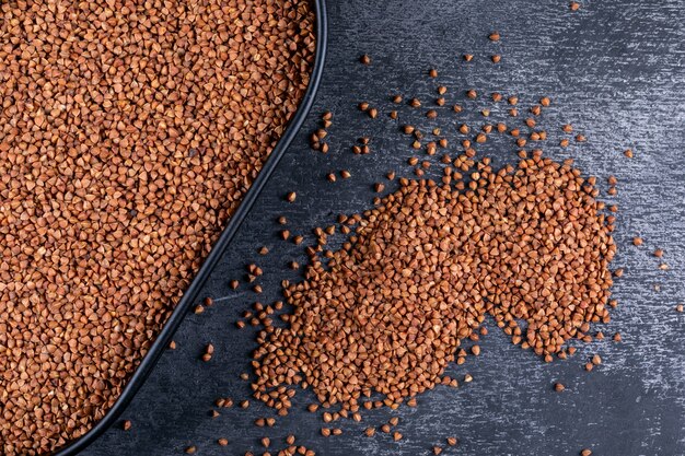 Top view buckwheats in a pot and alongside, on dark background. horizontal