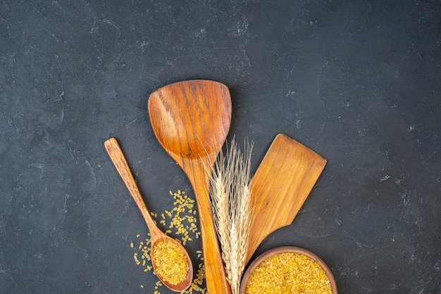 Top view bulgur wheat in bowl and wooden spoon two big wooden spoons wheat spikes on table free space