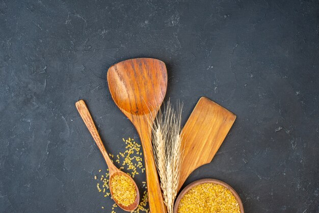 Top view bulgur wheat in bowl and wooden spoon two big wooden spoons wheat spikes on table free space