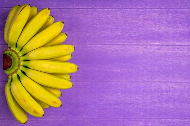 Top view of bunch of bananas isolated on purple wood with copy space