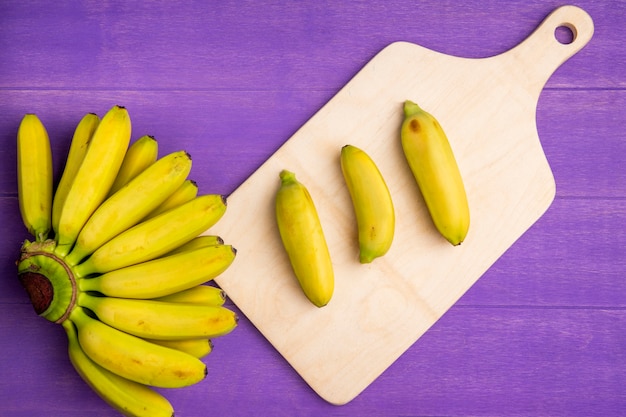 Top view of bunch of bananas on wood cutting board on purple wood