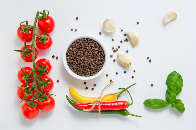 Top view a bunch of tomatoes with a bowl of black pepper, garlic, leaves, chili pepper on white background. horizontal