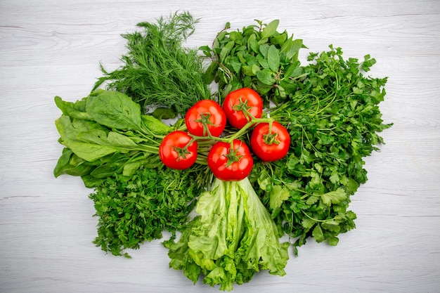 Top view of bundles of fresh greens and tomatoes with stem on white background