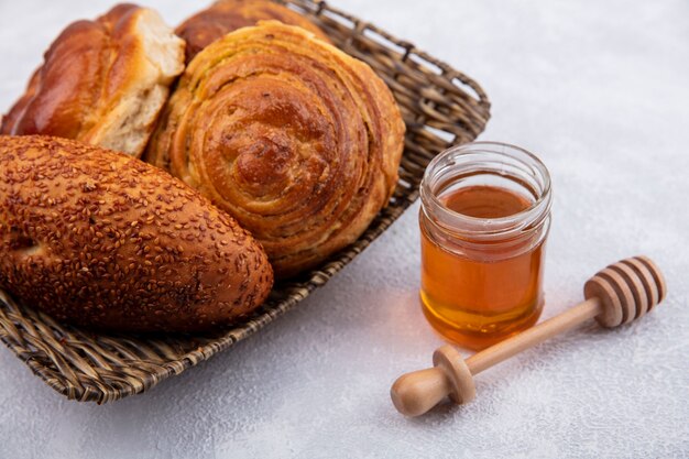 Top view of buns on a bucket with honey on a glass jar and wooden honey spoon on a white background