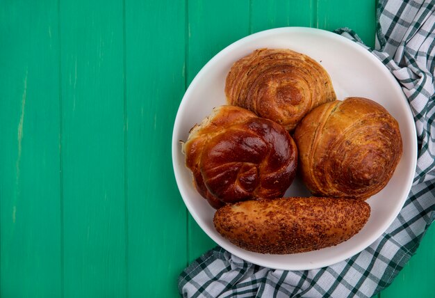 Top view of buns on a white plate on a checked cloth on a green wooden background with copy space