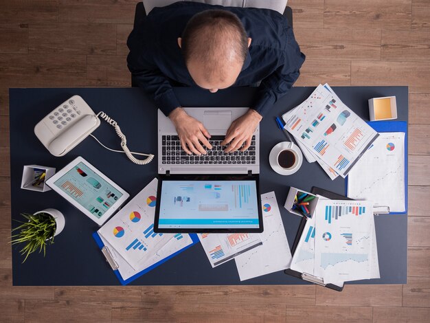 Top view of business man in corporate office sitting at desk, typing on laptop, working on financial statistics and business strategy