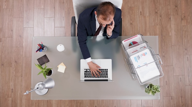 Top view of businessman discussing business profit with partner at phone while typing company statis...