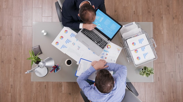 Top view of businessman showing management strategy presentation to partner discussing company statistics during business meeting. Businessmen working at financial graphs in startup office