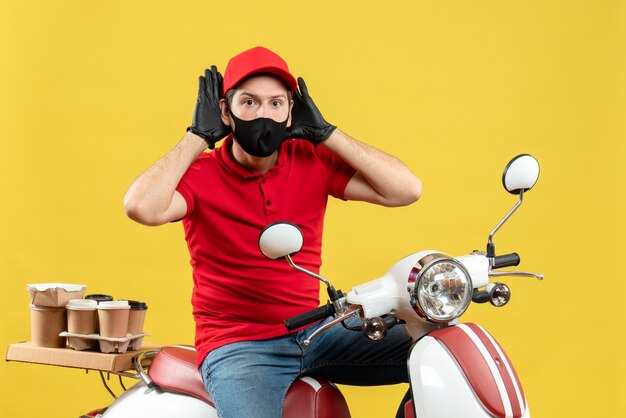 Top view of busy young adult wearing red blouse and hat gloves in medical mask delivering order sitting on scooter