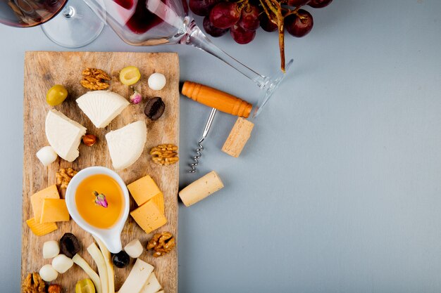 Free photo top view of butter with cheese grape olive nuts on cutting board and corkscrew corks on white with copy space