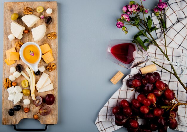 Top view of butter with cheese grape olive nuts on cutting board and glass of wine corks flowers on white