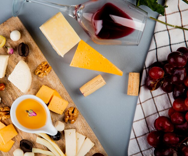 Top view of butter with cheese grape olive nuts on cutting board and glass of wine corks on white