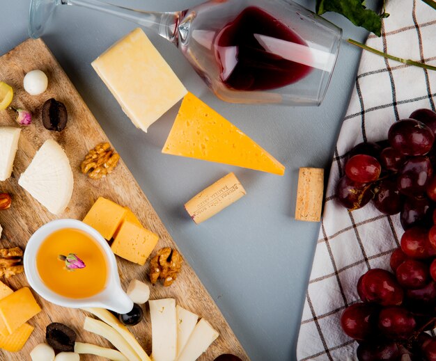 Вид сверху масла с сыром виноградных оливковых орехов на разделочной доске и бокал вина пробки на белом
