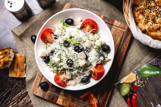 Top view of caesar salad bowl garnished with grated cheese and olive