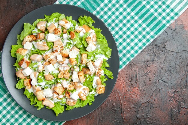 Top view caesar salad on oval grey plate green white checkered tablecloth on dark red background