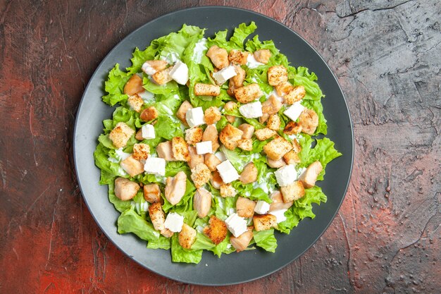 Top view caesar salad on oval plate on dark red background