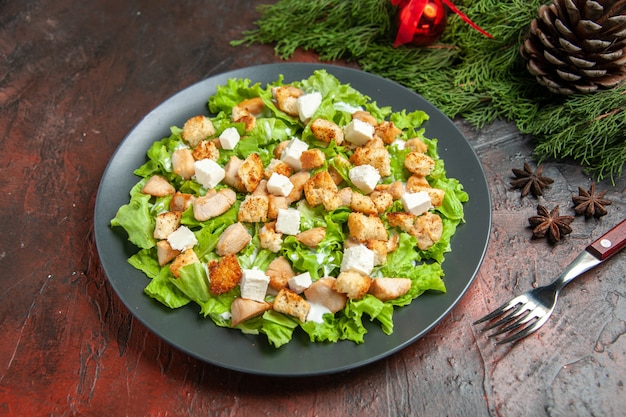 Top view caesar salad on oval plate fork anise seeds on dark red background