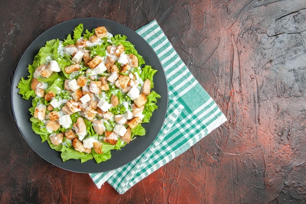 Vista dall'alto caesar salad su piatto ovale tovagliolo a scacchi bianco verde su sfondo rosso scuro