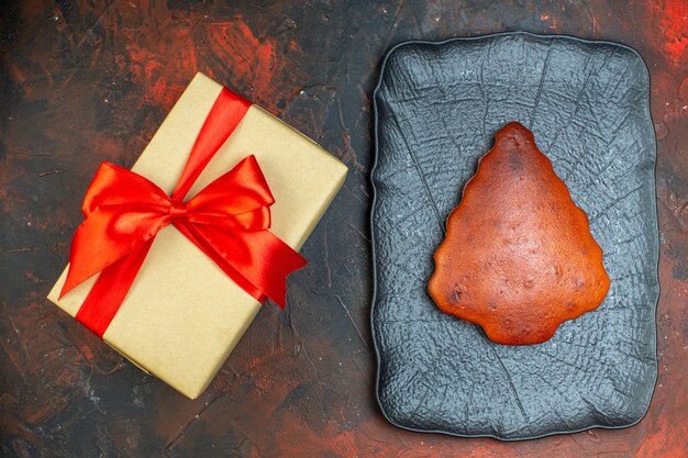 Top view cake on black platter gift tied with red ribbon on dark red table