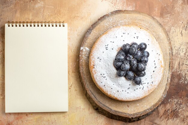 ケーキの上面図まな板の白いノートに黒ブドウとケーキ