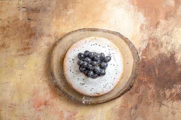 Top view of cake a cake with black grapes and powdered sugar on the cutting board