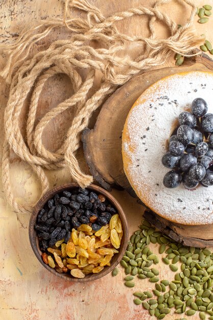 Free photo top view a cake a cake with grapes on the cutting board a bowl of raisins pumpkin seeds rope