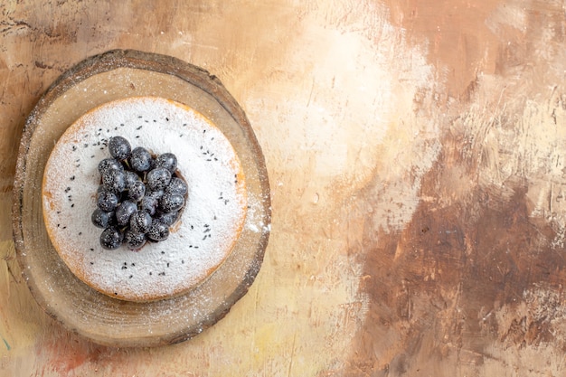 Top view of cake a cake with powdered sugar and black grapes on the cutting board