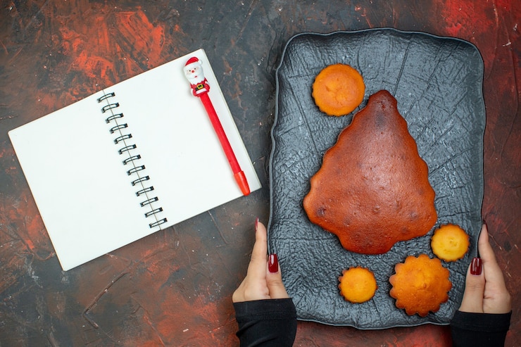 Free Photo top view cake and cupcakes on black plate in female hands pen on notebook on dark red table