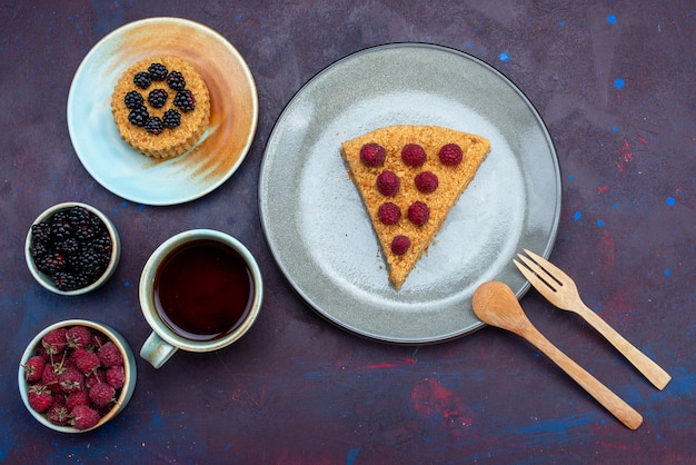 Vista dall'alto della fetta di torta deliziosa con lamponi all'interno del piatto con frutti di tè sulla superficie scura