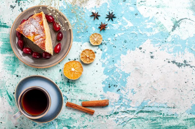 Top view cake slice wit fresh red dogwoods and cup of tea on blue background fruit cake bake pie biscuit sweet