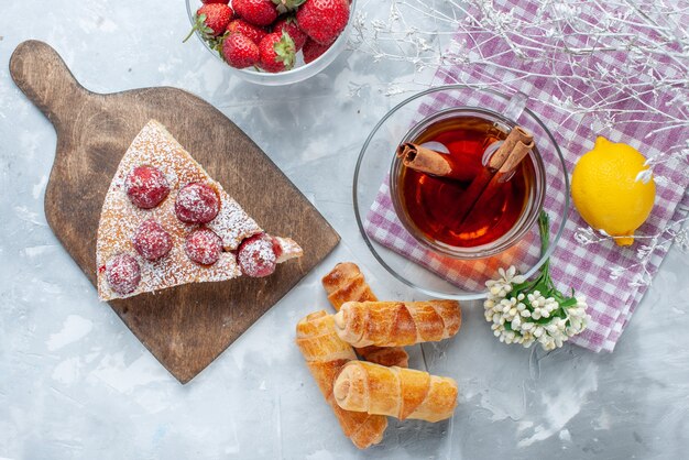 Top view of cake slice with fresh red strawberries sweet bangles and tea on light desk, sweet bake biscuit cookie tea pastry