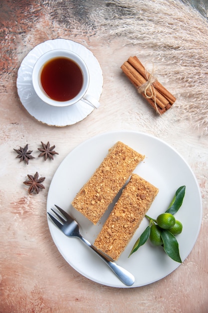 Top view cake slices honey cake with cup of tea on light floor sweet pie biscuit cake