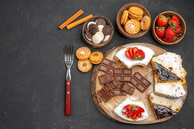 暗い机の上にクッキーとチョコレートとトップビューのケーキのスライス