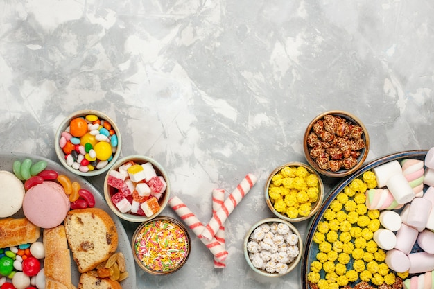 Top view of cake slices with french macarons bagels and candies on white wall