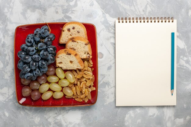 Top view cake slices with grapes and raisins inside red plate on the white surface