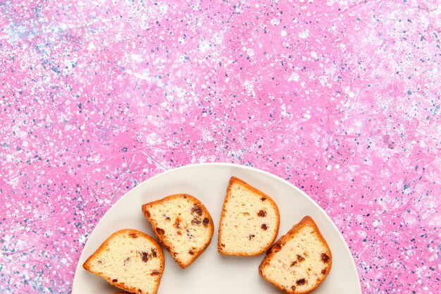 Вид сверху кусочки торта с изюмом внутри тарелки на розовом фоне выпечка торта сладкого бисквитного цвета сахарное печенье