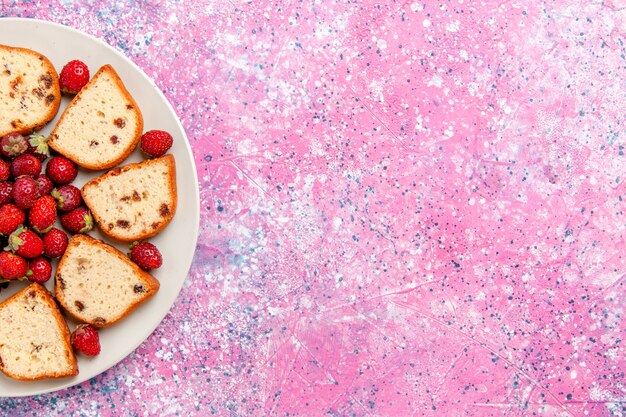 Вид сверху на кусочки торта с изюмом внутри тарелки со свежей клубникой на светло-розовом письменном торте Выпечка сладкого бисквитного цвета пирог сахарное печенье