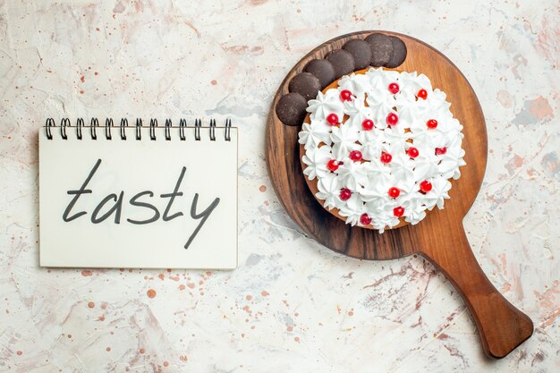 Foto gratuita torta vista dall'alto con cioccolato e crema pasticcera bianca su tagliere in legno. gustoso scritto sul taccuino